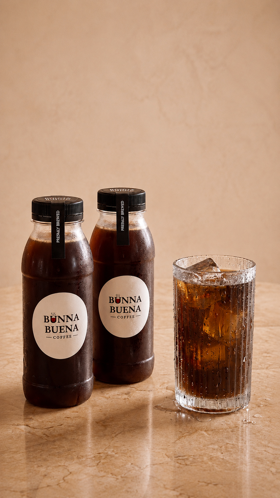 Two Bunna Buena cold brew bottles and a glass of iced black cold brew on warm stone